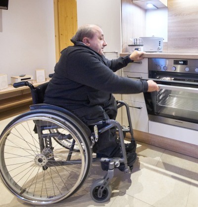Ein Rollstuhlfahrer macht in der Küche den Ofen auf. 
