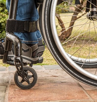 Ansicht der Räder eines Rollstuhls und der Beine eines Menschen. 