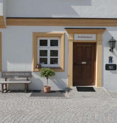 Behindertenrechter Eingang der Stadtbücherei Altötting mit einer Sitzbank an der Hausmauer.