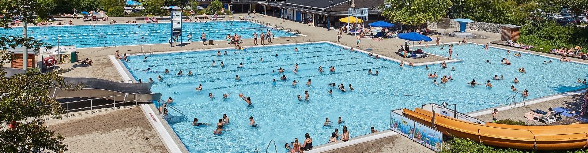 Das Schwimmbecken mit Rutsche im Freibad St. Georgen in Altötting ist voller Menschen.