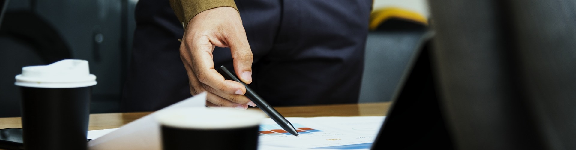 Ein Hand deutet mit einem Stift auf ein Blatt Papier und scheint mitten in einer Besprechung zu sein.  