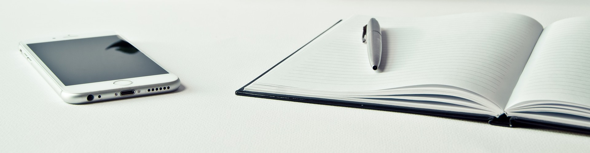 Ein Notizbuch sowie ein Handy liegen auf einer weißen Schreibtischplatte. 