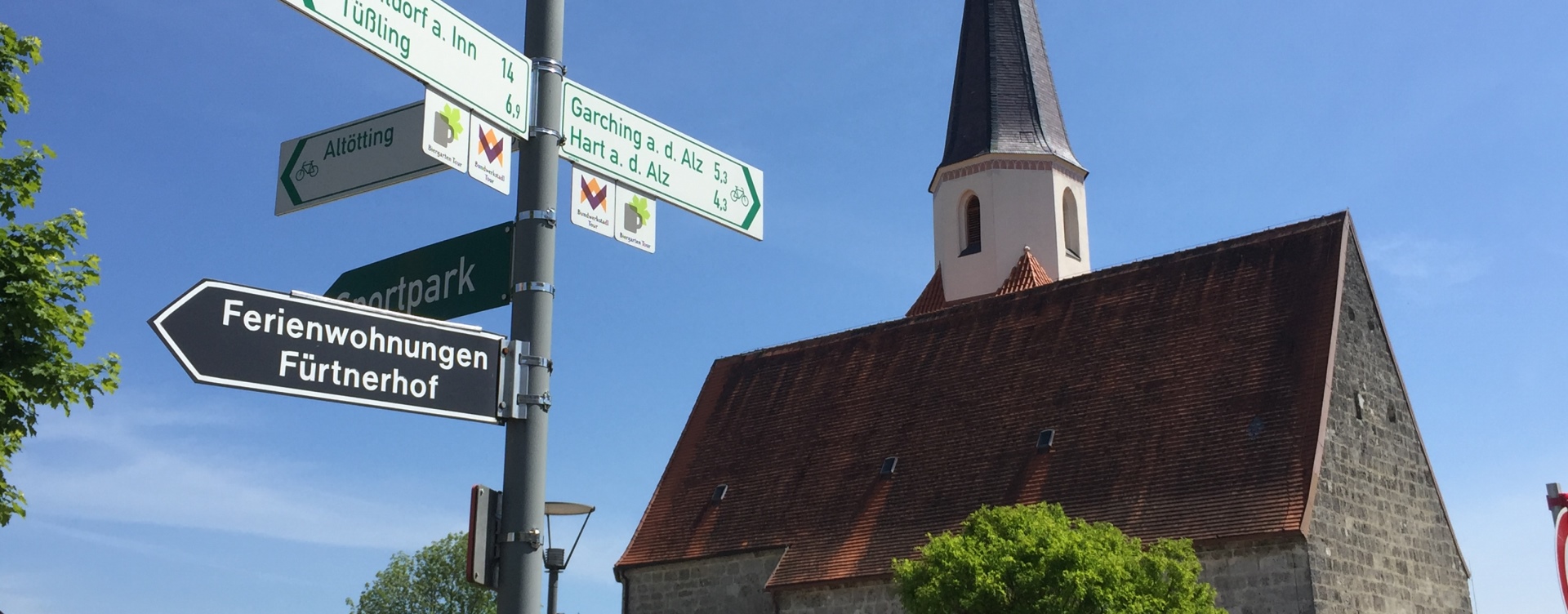 Hier sehen Sie die Kirche in Unterneukirchen mit den Schildern der Fahrradregion Inn-Salzach 