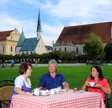 Drei Menschen sitzen auf dem Kapellplatz vor der Gnadenkapelle bei Kaffee und Kuchen zusammen.