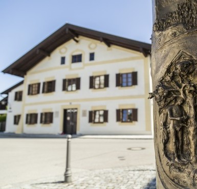 Im Hintergrund befindet sich das Geburtshaus von Papst Benedikt XVI. in Marktl am Inn, im Vordergrund die Papstsäule.