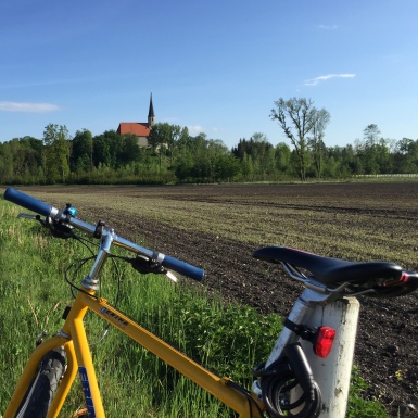 Hier sieht man die Kirche von Mauerberg in der Ferne mit einem Fahrrad im Vordergrund