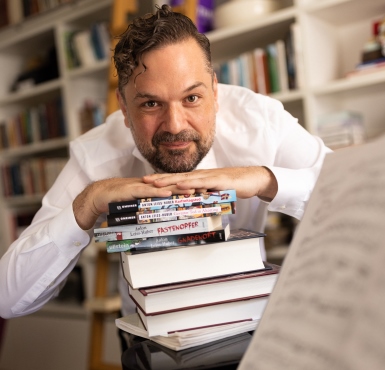 Anton Leiss-Huber lehnt auf einem Stapel seiner veröffentlichten Bücher. 