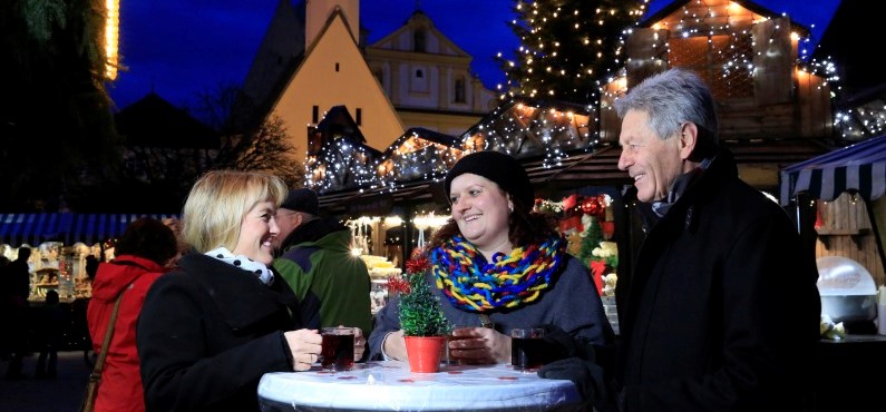 Besucher des Altöttinger Christkindlmarktes, die an einem Tisch zusammenstehen.