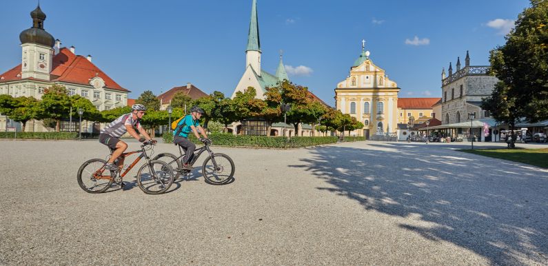 Hier sehen Sie zwei Fahrradfahrer am Kapellplatz vor der Gnadenkapelle