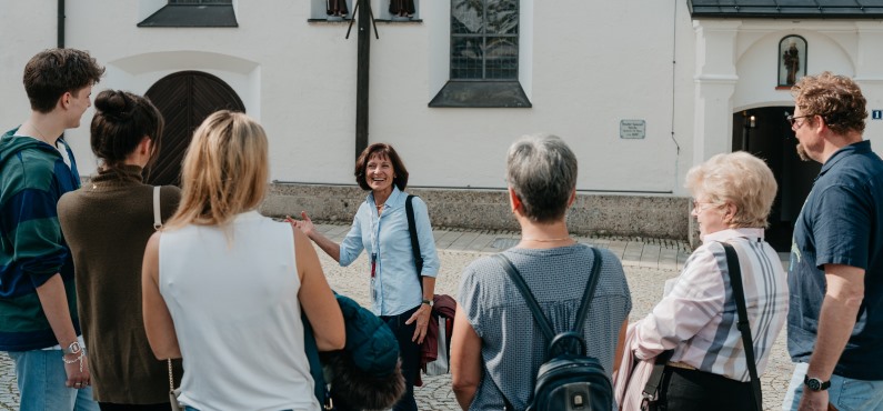 Eine Stadtführerin steht vor ihrer Gruppe und lacht. 