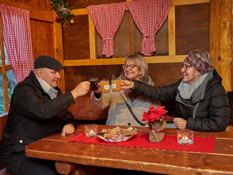 Drei Menschen stoßen mit einer Tasse Glühwein am Tisch an. 