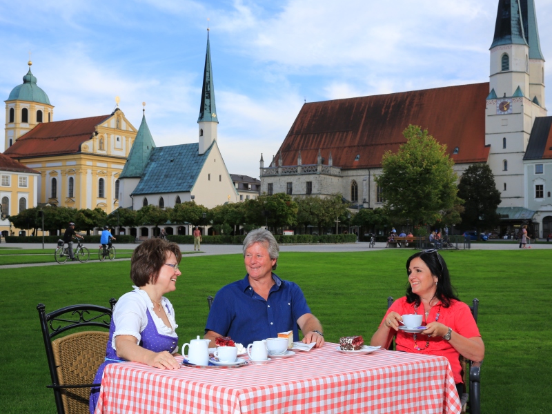 Drei Menschen sitzen am Kapellplatz an einem Tisch bei Kaffee und Kuchen. 