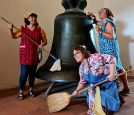 Drei Frauen putzen eine große Glocke.