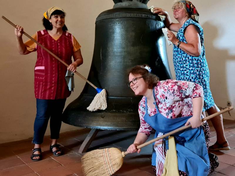 Drei Frauen putzen eine große Glocke.