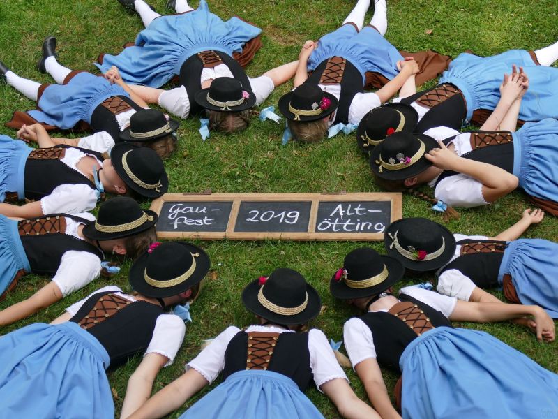 Trachtlerinnen liegen im Kreis mit Hüten über dem Kopf.