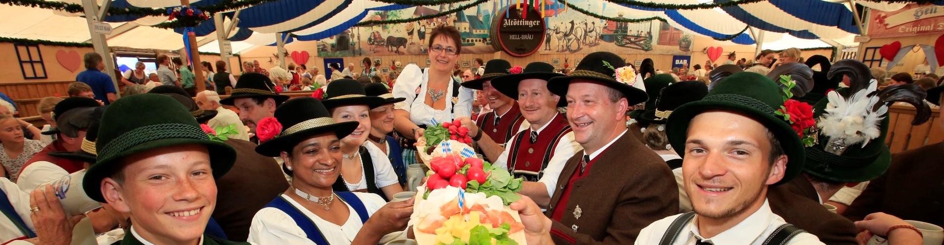 Eine Gruppe, die in dem Festzelt auf der Alöttinger Hofdult eine Brotzeitplatte am Tisch hochhebt.