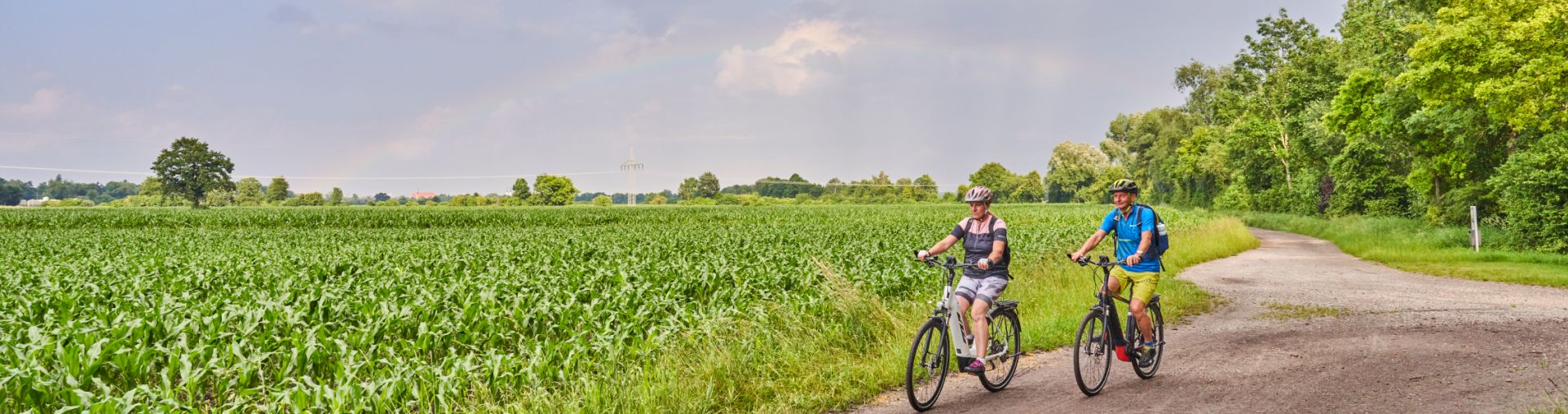 Hier sehen Sie zwei Fahrradfahrer mit Regenbogen im Hintergrund