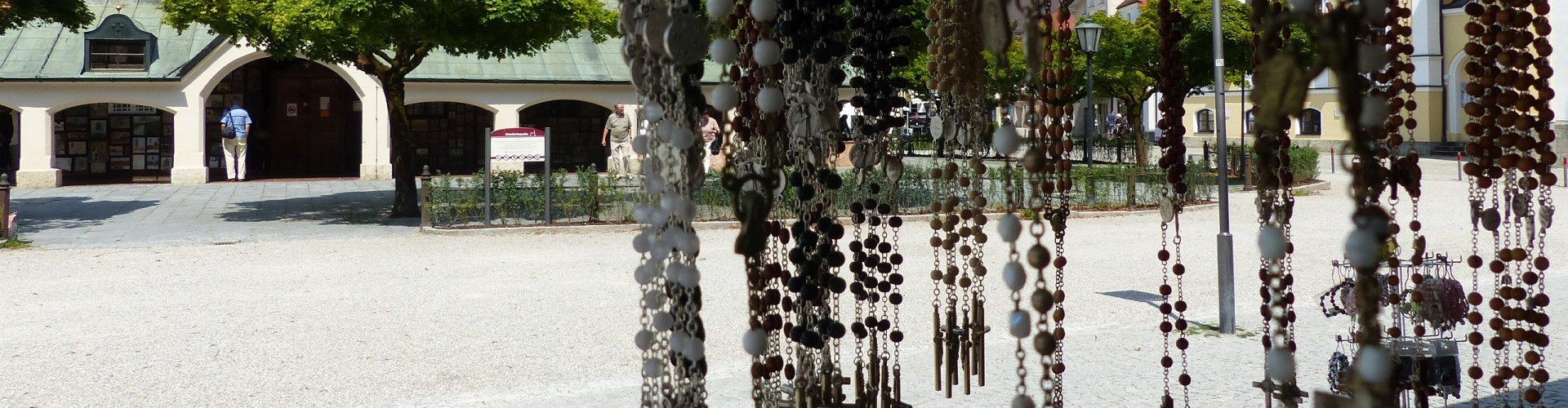 Verschiedene Rosenkränze von einem Geschäft am Altöttinger Kapellplatz mit Blick auf die Gnadenkapelle.