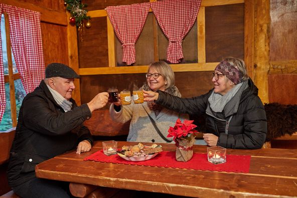 Zwei Frauen und ein Mann sitzen in einer urigen Hütte und trinken Glühwein.