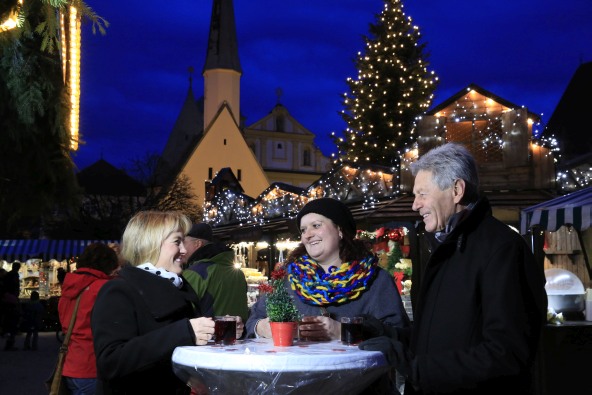Eine kleine Besuchergruppe steht auf dem Altöttinger Christkindlmarkt gemütlich beisammen.