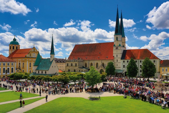 Der Altöttinger Kapellplatz mit einigen Pilgern gefüllt, die rund um die Gnadenkapelle stehen.