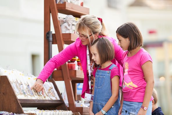 Eine Stadtführerin erklärt zwei Kindern eine Kerze. 