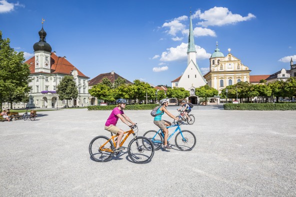 Ein paar Radfahrer auf dem Altöttinger Kapellplatz, vor der Gnadenkapelle.