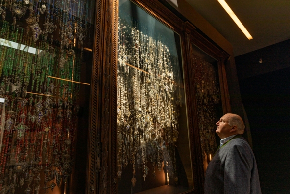 Ein Mann steht vor einer Vitrine voller Rosenkränze. 