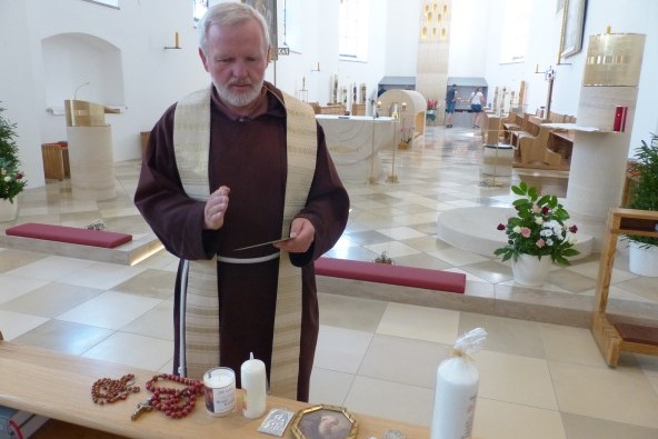 Ein geistlicher segnet verschiedene Andachtsgegenstände, wie einen Rosenkranz, Kerzen und Anhänger in der Altöttinger St. Kornrad Kriche.