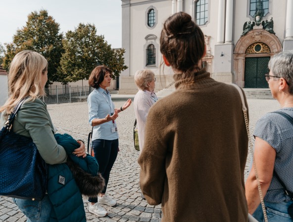 Eine Stadtführerin steht vor der Basilika und erklärt ihrer Gruppe etwas.