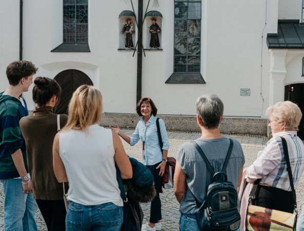 Eine Stadtführerin steht lachend vor ihrer Gruppe.