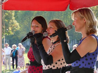 Drei Damen in gepunkteten Kleidern singen ins Mikrofon.