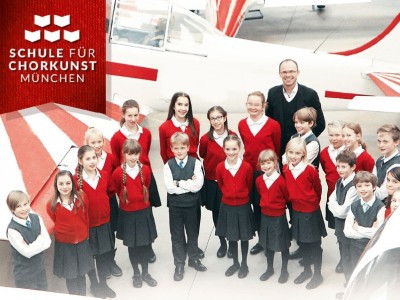 Der Münchner Kinderchor steht vor einem Modellflugzeug. 